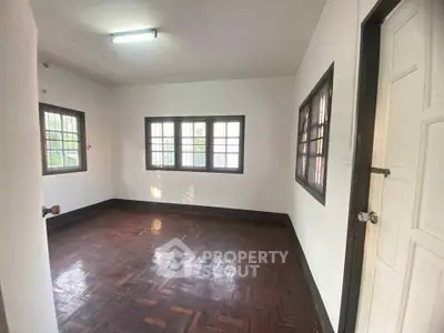 Spacious empty room with wooden flooring and large windows, perfect for customization.