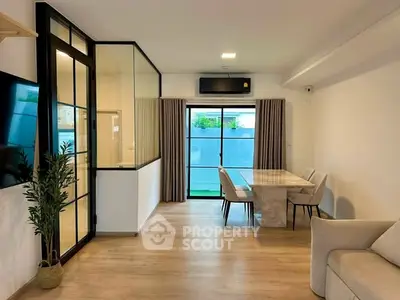 Modern living room with glass partition and stylish dining area, featuring sleek furniture and natural light.