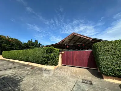 Charming suburban home with lush hedges and a gated entrance under a clear blue sky.