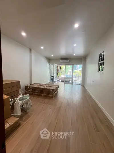Spacious unfurnished living room with wooden flooring and large windows leading to a balcony.