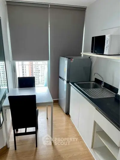 Modern kitchen with dining area, featuring fridge and microwave, in a high-rise apartment.