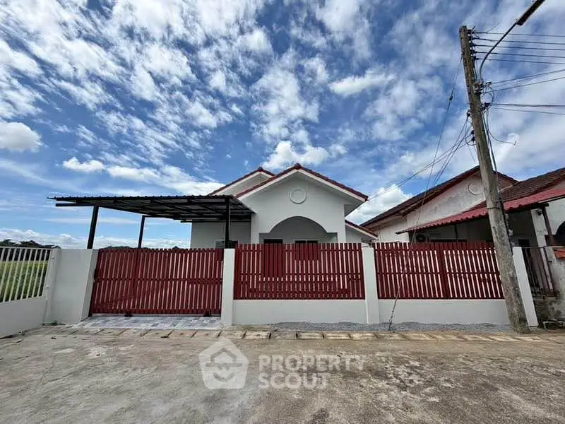 Charming single-story house with red fence and carport under a vibrant blue sky.