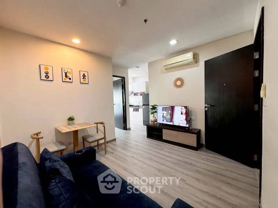 Modern living room with stylish decor and open view to kitchen area, featuring cozy seating and wall-mounted TV.
