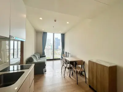 Modern living room with open kitchen and city view, featuring sleek furniture and natural light.