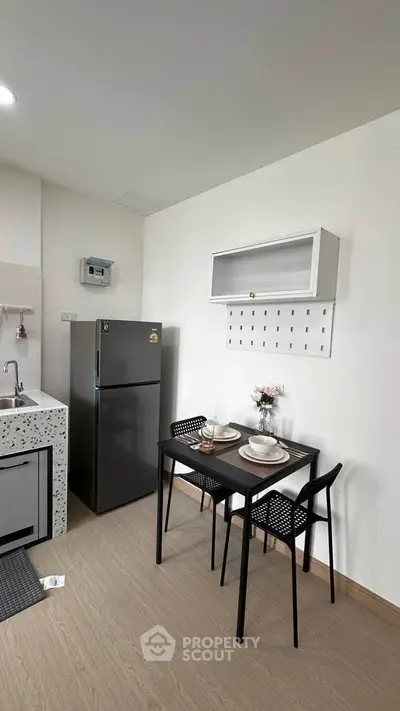 Modern kitchen with dining area, featuring sleek black table and chairs, stainless steel fridge, and minimalist decor.