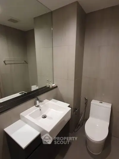 Modern bathroom with sleek fixtures and minimalist design, featuring a square sink and contemporary toilet.