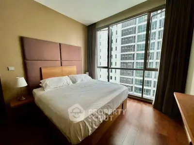 Modern bedroom with large window and city view, featuring a cozy bed and wooden flooring.