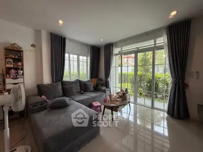 Spacious living room with large windows and garden view, featuring modern gray sectional sofa and elegant decor.