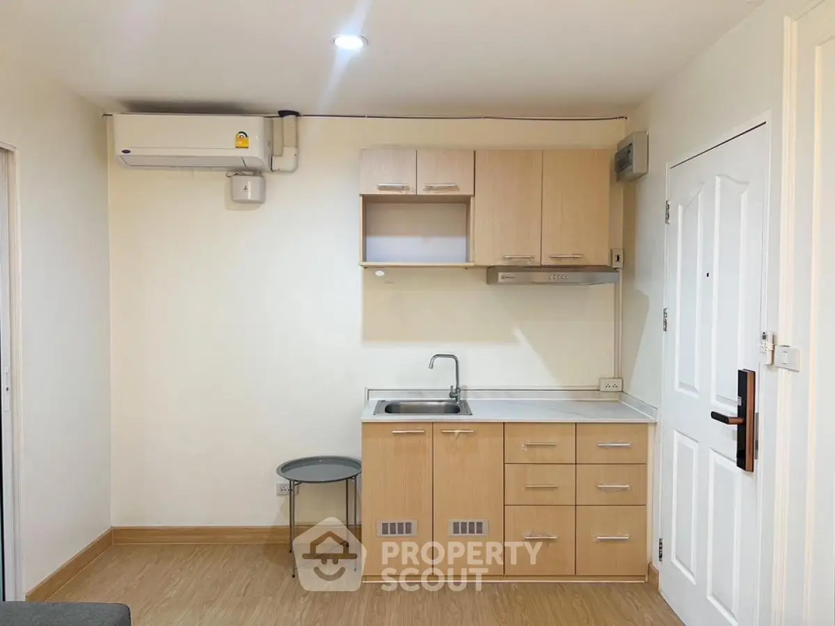 Compact kitchen area with modern cabinetry and air conditioning in cozy apartment