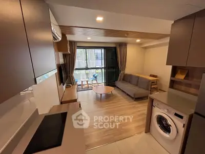 Modern living room with open kitchen and washing machine, featuring large windows and stylish furnishings.