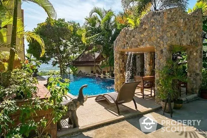 Luxurious tropical poolside retreat with lush greenery and stone waterfall feature.