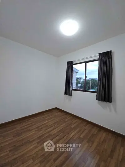 Spacious bedroom with wooden flooring and large window for natural light.