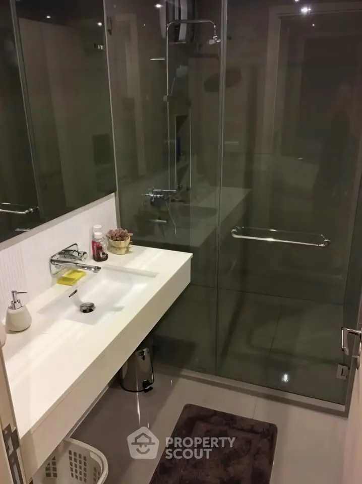 Modern bathroom with glass shower and sleek white sink in contemporary apartment.
