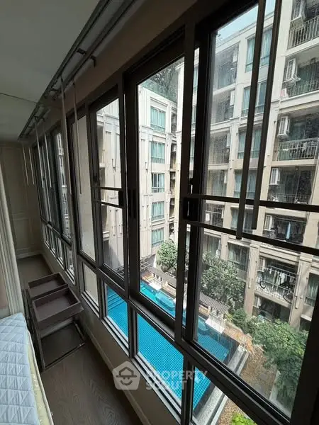 Spacious apartment with large windows overlooking a pool and modern building.