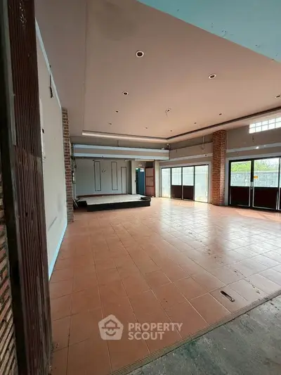 Spacious open-plan room with tiled flooring and large windows, ideal for versatile use.