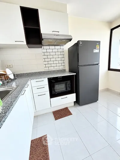 Modern kitchen with sleek black fridge and built-in oven in bright apartment.