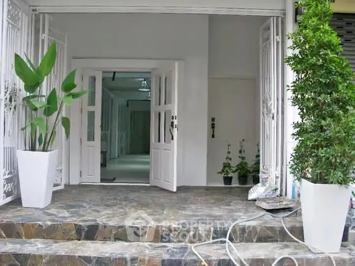 Charming entrance with elegant potted plants and stone steps leading to a welcoming doorway.