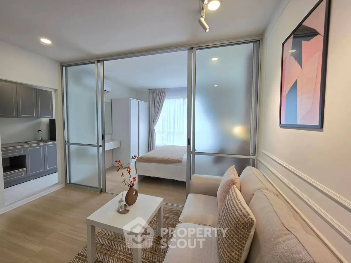 Modern studio apartment with cozy living area and stylish bedroom separated by glass partition.