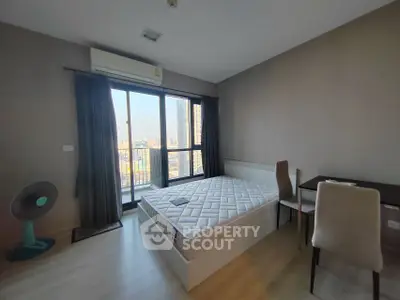 Modern bedroom with city view, featuring a bed, desk, and large window for natural light.