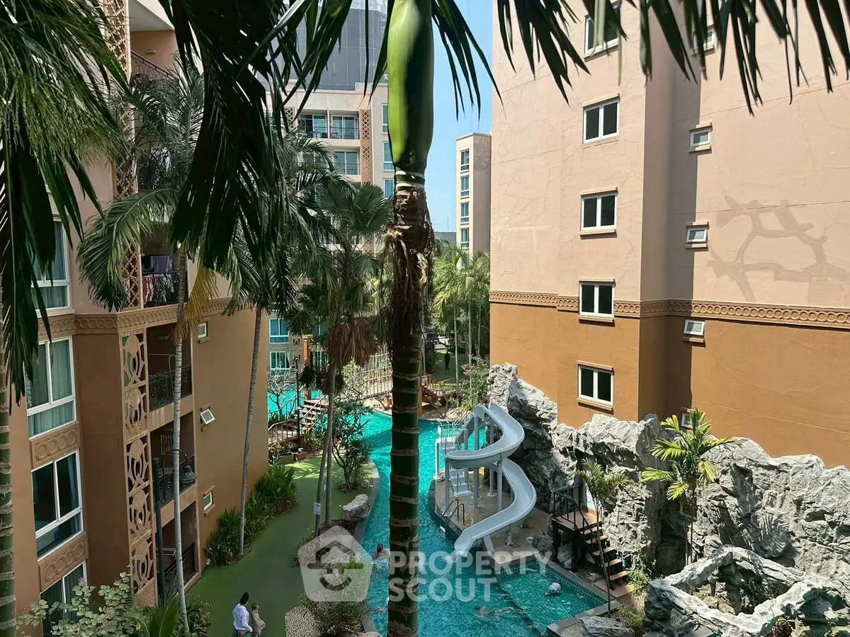Luxurious apartment complex with pool and water slide, surrounded by lush greenery.
