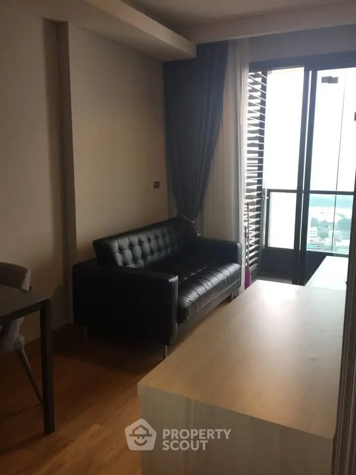 Modern living room with sleek black sofa and balcony view, perfect for urban living.