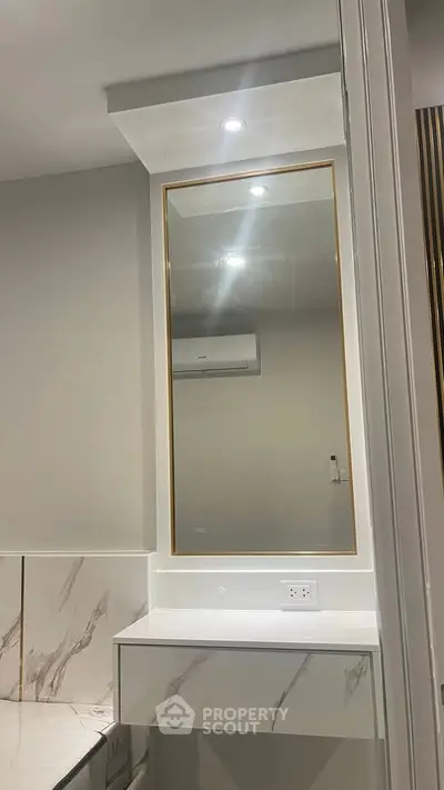 Modern bathroom with elegant mirror and marble accents, featuring sleek lighting and contemporary design.
