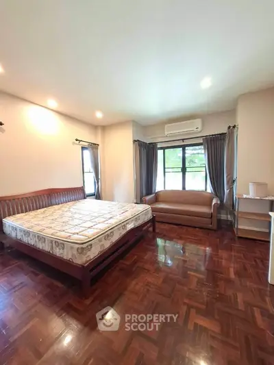 Spacious bedroom with wooden flooring and large windows in a modern apartment.