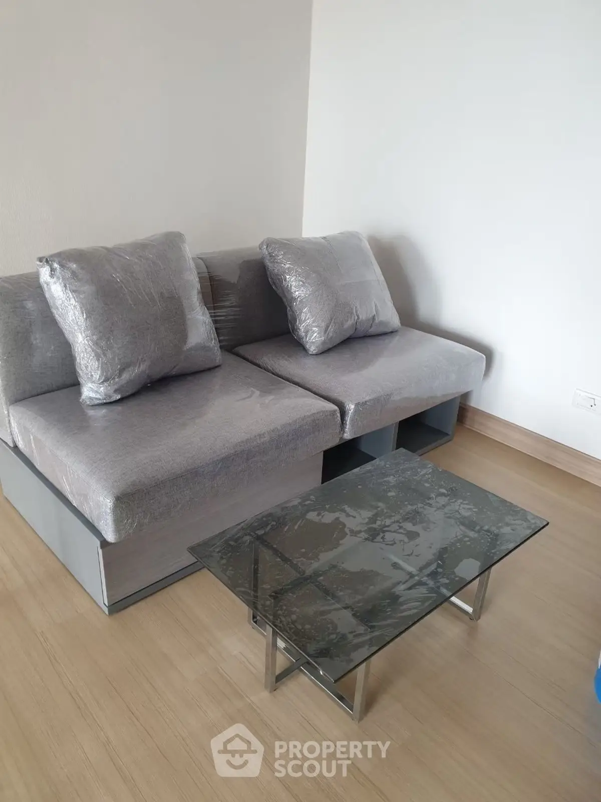 Modern living room with sleek gray sofa and glass coffee table on wooden floor.