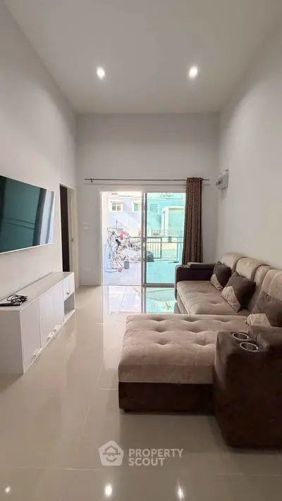 Modern living room with plush sofa and large TV, leading to a bright balcony view.