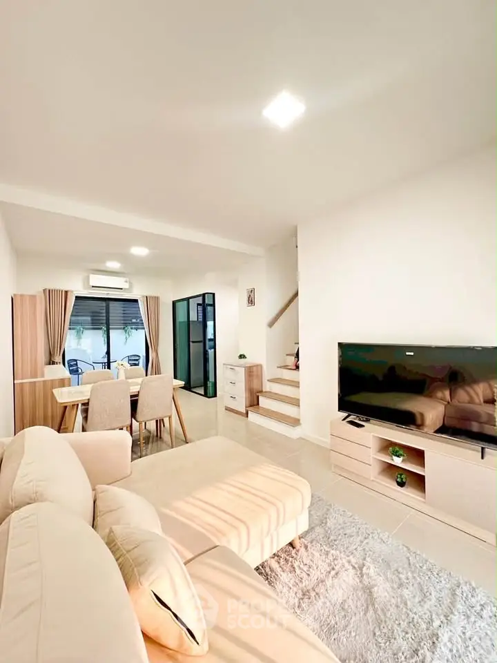 Spacious living room with modern decor and dining area, featuring a cozy beige sofa and large flat-screen TV.