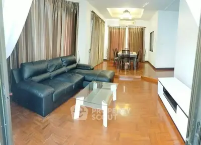 Spacious living room with elegant black leather sofa and dining area, featuring polished wooden floors and ample natural light.