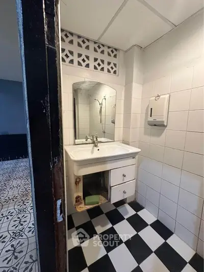 Compact bathroom with checkered floor and wall-mounted sink in real estate property.