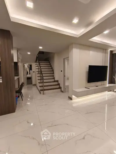 Modern living room with sleek staircase and TV, featuring elegant lighting and glossy tile flooring.