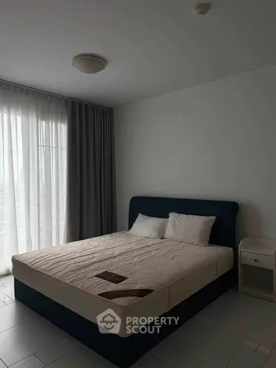 Spacious bedroom with large window and modern furnishings in a stylish apartment.