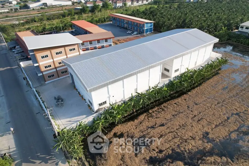 Aerial view of a modern industrial warehouse with adjacent office buildings and lush surroundings.