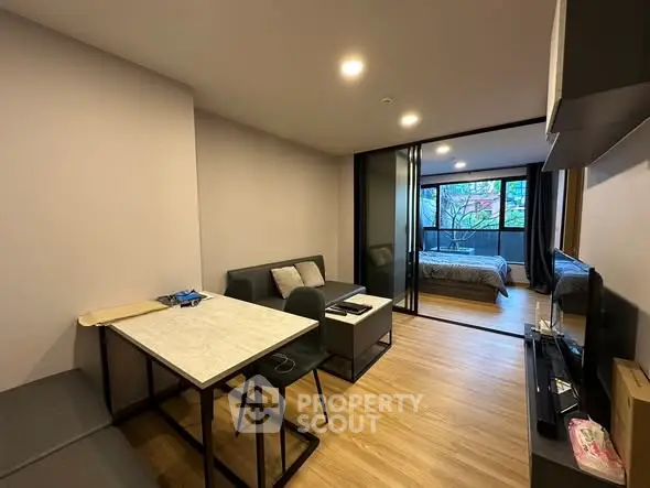Modern apartment with open living and bedroom space, featuring sleek furniture and large windows.