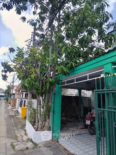 Charming residential street view with vibrant green house and lush trees, perfect for serene living.