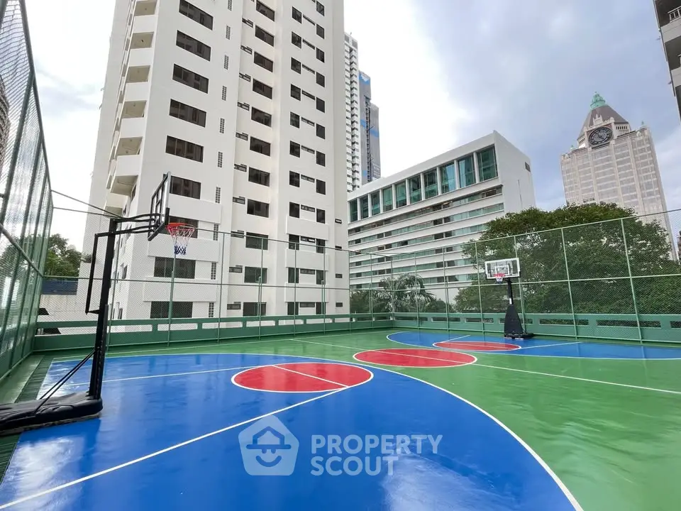 Modern urban apartment complex with vibrant outdoor basketball court and city skyline view.