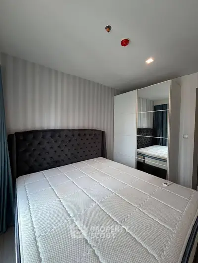 Modern bedroom with plush headboard and mirrored wardrobe in stylish apartment.