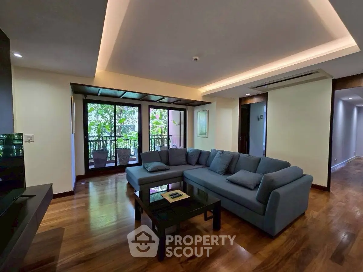 Spacious living room with modern decor and large windows opening to a lush balcony view.