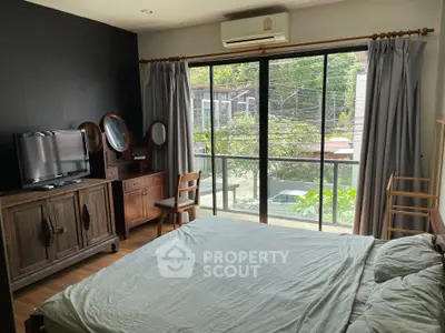 Cozy bedroom with balcony view, featuring wooden furniture and natural light.