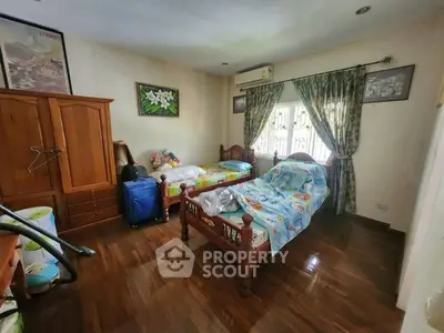 Cozy bedroom with wooden flooring and classic furniture, featuring a single bed and large window with curtains.