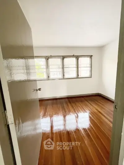Spacious bedroom with polished wooden floors and large windows for natural light.