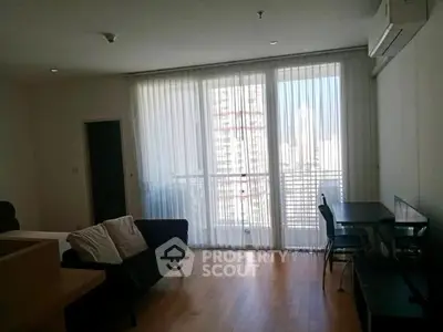 Spacious living room with large windows and city view, featuring modern furniture and wooden flooring.