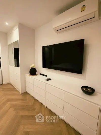 Modern living room with sleek white cabinetry and wall-mounted TV, featuring elegant wood flooring and air conditioning.