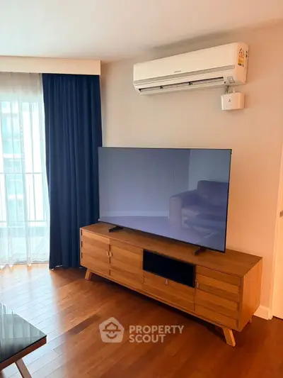 Modern living room with sleek TV setup and air conditioning, featuring elegant wooden flooring and stylish curtains.