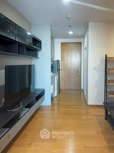 Modern apartment interior with sleek wooden flooring and built-in entertainment unit, featuring a compact kitchen area.