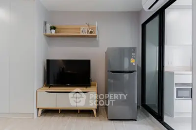 Modern living room with sleek TV stand and stainless steel fridge, adjacent to a stylish kitchen.