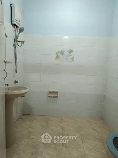 Simple bathroom with tiled walls and floor, featuring a sink and shower area.