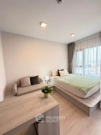 Modern bedroom with cozy bed, stylish sofa, and large window offering natural light and city views.